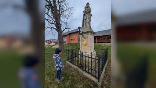 Ein Kind vor einer Marienstatue, die mit einem niedrigen Gitter eingezäunt ist.