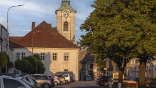 Blick auf einen Marktplatz mit Kirche im Abendlicht. Zahlreiche geparkte Autos.