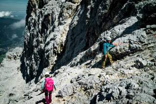 Zwei Bergsteiger mit Helmen und Rucksäcken klettern an steilen, felsigen Klippen in den Bergen.