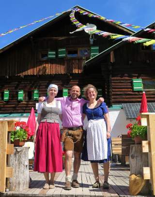 Zwei Frauen und Mann stehen in Tracht vor Berghütte