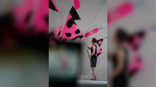 Ein Mann reinigt mit einem langen Werkzeug bunte, pink-schwarze Klettergriffe an einer Kletterwand.