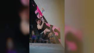 Junger Mann klettert an einer Indoor-Bouldering-Wand mit auffälligen pink-schwarzen Griffen.