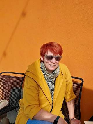 Melanie Grimm sitzt vor einer orangen Hauswand.