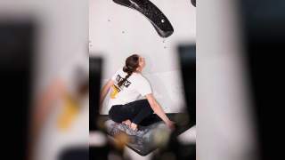 Frau beim Bouldern an einer Kletterwand mit großen schwarzen Griffen, die konzentriert nach oben blickt.