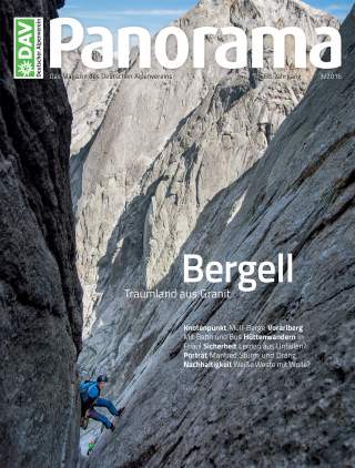 Bergsteiger klettert zwischen steilen Granitfelsen in einer engen Felsspalte, im Hintergrund hohe, zerklüftete Bergwände.