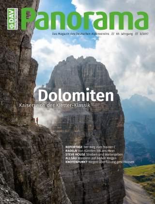 Magazine-Cover mit beeindruckender Felswand in den Dolomiten und einer kleinen Person in roter Jacke, die auf einer Klippe steht, umgeben von Wolken und Bergen im Hintergrund.